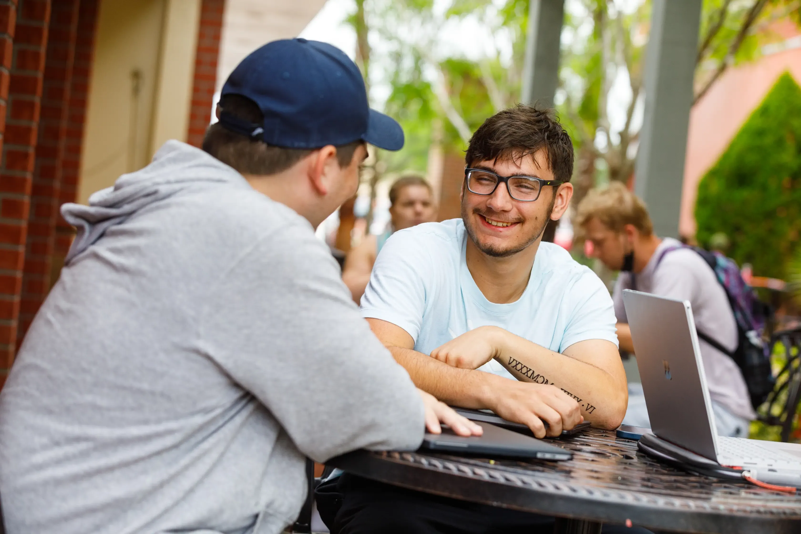 一名戴眼镜的男学生微笑着与另一名戴蓝色棒球帽的学生坐在一起